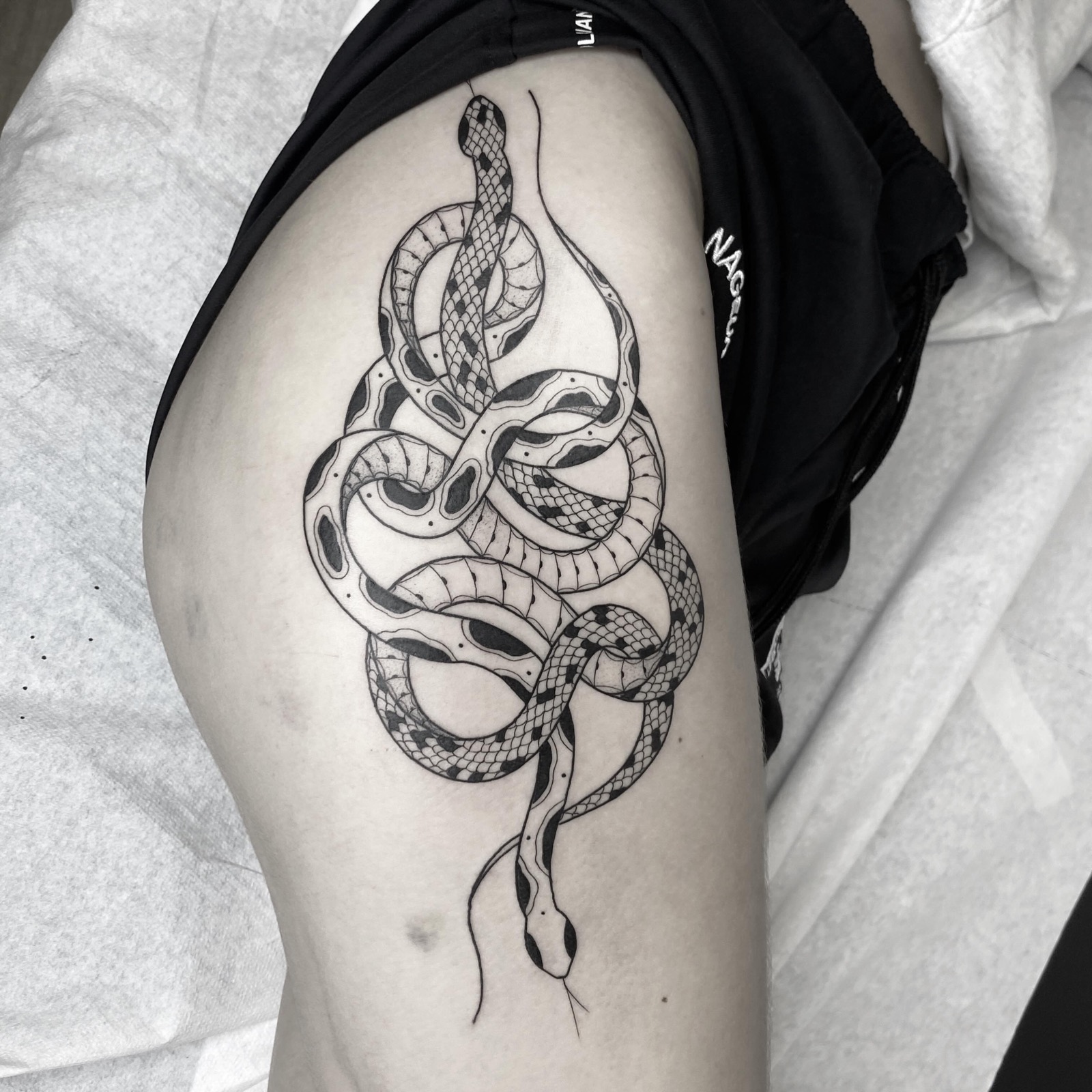 Deux serpents enlacés en blackwork sur la cuisse